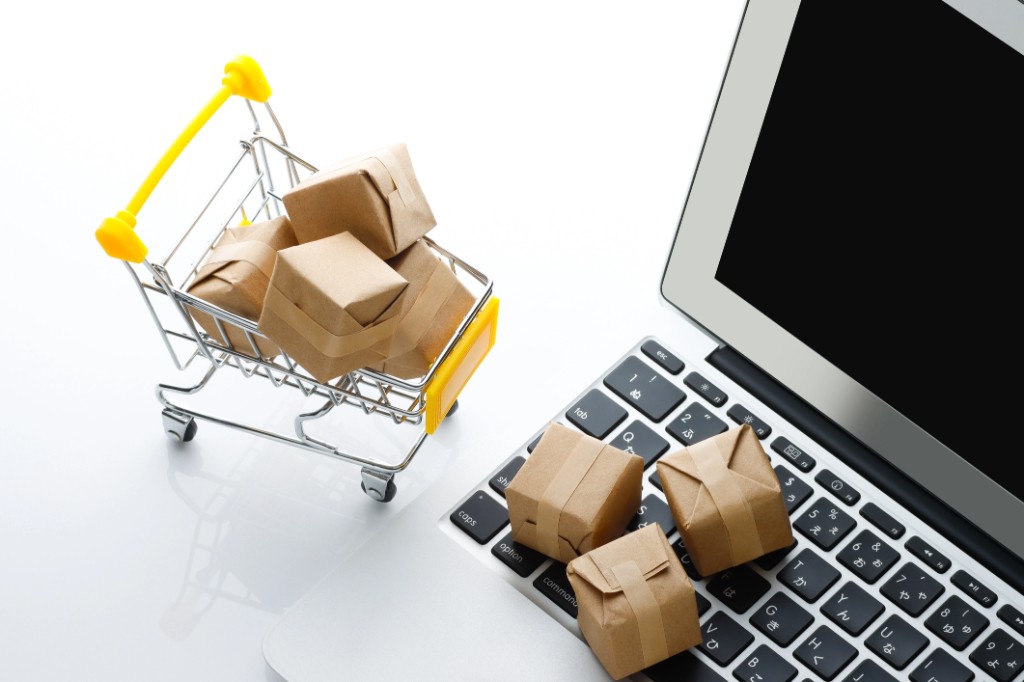 Carrito de compras con paquetes junto a un portátil: comercio online